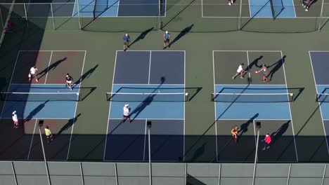 Multiple-games-of-pickleball-at-local-club,-players-on-courts-in-teams-of-two,-aerial-orbit
