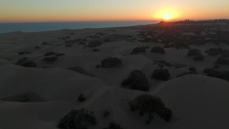 flying-over-the-dunes-of-Maspalomas-beach-during-the-sunset-and-with-the-Maspalomas-lighthouse-as-a-background