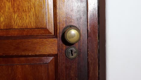 Man-with-a-black-glove-on-slowly-opens-a-brass-door-knob-on-a-wooden-door