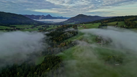Aerial-drone-shot-over-white-clouds-passing-over-a-mountain-town-along-the-mountain-valley-covered-with-green-vegetation-during-evening-time