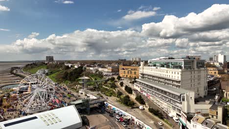 Drone-shot-shows-Southend-On-Sea,-Essex,-seaside-funfair-Adventure-Island,-Royal-Hotel,-The-Royals-Shopping-Centre-and-people-enjoying-the-rides-and-promenade