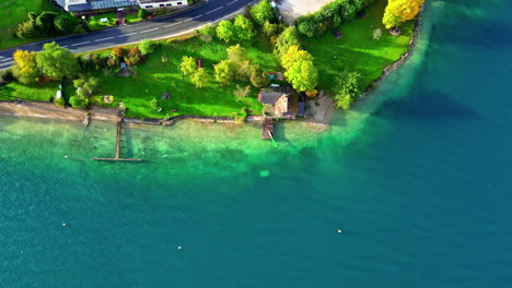 Aerial-drone-top-down-shot-over-wooden-cottages-surrounded-by-beautiful-blue-lake-water-during-morning-time