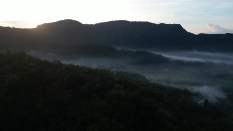 Ein-Nebliger-Sonnenaufgang-über-Dem-Osten-Von-Bali-Mit-Bergen,-Die-Die-Landschaft-Umgeben,-Aus-Der-Luft