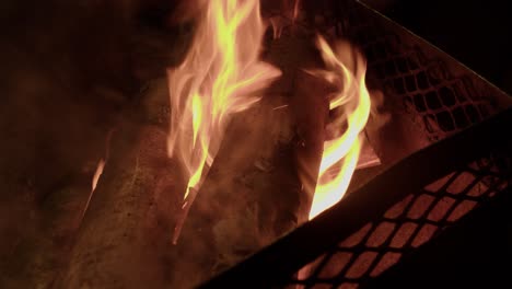 Birch-logs-burn-in-metal-fire-box-flames-at-campsite-on-dark-night