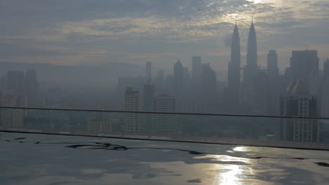 Vista-De-La-Ola-Sobre-El-Agua-En-Primer-Plano-Y-El-Paisaje-De-La-Ciudad-En-La-Niebla-En-El-Cielo-Nublado-Y-El-Sol-Kuala-Lumpur-Malasia