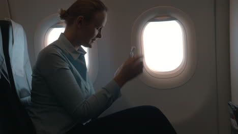 En-La-Cabina-Del-Avión,-Una-Chica-Sentada-En-Una-Silla-Y-Usando-Un-Terminal-Móvil-En-El-Teléfono-Y-Paga-La-Compra-Con-Tarjeta.