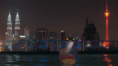 Woman-with-pad-in-rooftop-pool-of-night-Kuala-Lumpur