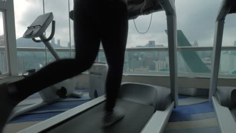 Close-up-view-of-woman-on-the-treadmill-in-fitness-centre-looking-at-window-with-cityscape-Hong-Kong-China