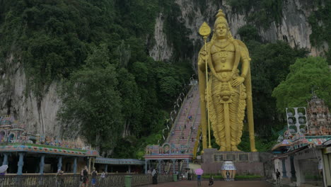 Vista-De-La-Entrada-En-La-Escalera-De-Las-Cuevas-De-Batu-Y-La-Estatua-De-Oro-De-Murugan-Contra-La-Montaña-Gombak-Selor-Malasia