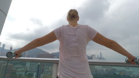 In-Hong-Kong-China-on-the-terrace-a-young-girl-does-exercises-with-dumbbells-spreading-hands