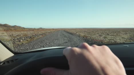 Point-of-view-of-driver-holding-steering-wheel,-driving-on-gravel-road