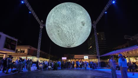 Große-Helle-Mondkunstausstellung-Auf-Dem-Stadtplatz-Bei-Nacht,-Menschen-Machen-Selfies-Mit-Supermond,-Zeitraffer