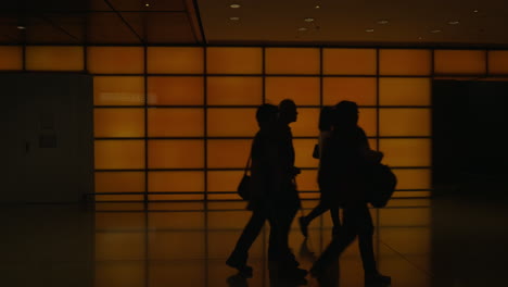Going-people-with-luggages-along-hall-against-illuminated-orange-wall