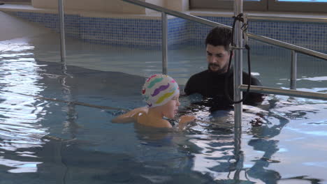 En-La-Clínica-Médica-Evexia-En-La-Piscina,-El-Médico-Busca-A-Un-Niño-Que-Nada-Y-Sostiene-La-Barandilla.