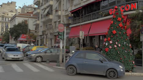 An-Der-Straße-Stehen-Ein-Weihnachtsbaum-Und-Ein-Geparktes-Auto,-Dann-Warten-An-Der-Kreuzung-Fußgänger-Und-Autos