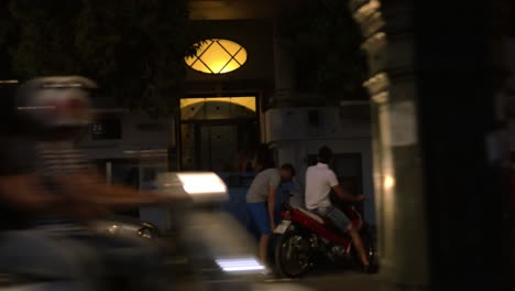 Por-La-Noche,-Ciudad-Por-La-Carretera-Pasando-Coches,-Motociclistas,-Gente-Caminando.