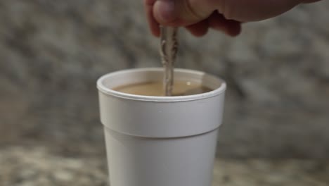 A-man-stirs-their-coffee-with-a-silver-spoon-in-a-styrofoam-cup