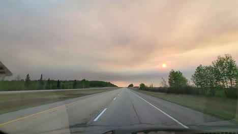 Car-driving-along-highway-while-sun-is-setting-on-the-horizon,-Canada