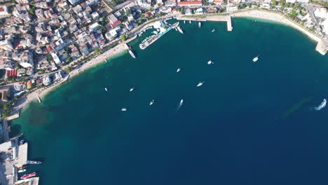 Breathtaking-Aerial-Panorama:-Saranda's-Coastal-City,-a-Tranquil-Tourist-Haven,-Showcasing-a-Pristine-Blue-Bay-Meeting-the-Deep-Blue-Sea