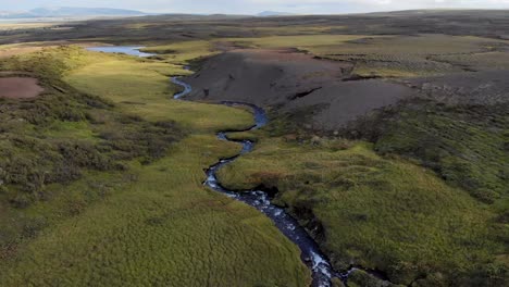 Aerial-of-a-winding-river-in-an-green,-hilly-landscape-in-Iceland