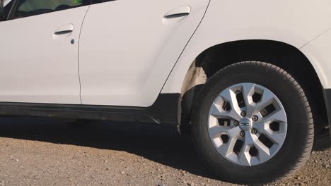 Left-rear-wheel-and-tire-of-white-car-starting-to-drive-on-gravel-road