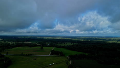 Drone-rises-above-farmland-forest-up-to-thick-dense-grey-clouds-in-sky