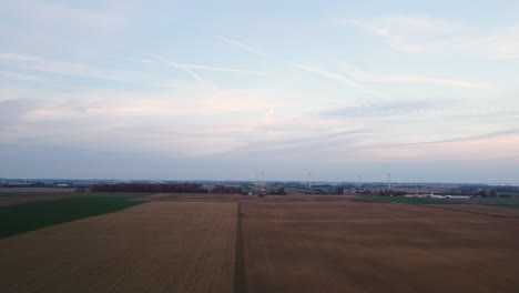 Panoramic-aerial-above-agricultural-fields-with-turbines-in-the-distance,-overcast-day