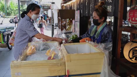 Woman-pays-the-fruit-vendor-then-takes-more-to-buy,-Street-Food-along-Sukhumvit-Road-in-Bangkok,-Thailand