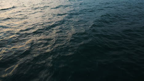 Sunset-golden-light-spread-on-deep-dark-blue-ocean-water-texture,-aerial-bird's-eye-view