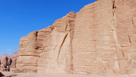 Massive-sandstone-blocks-create-sheer-cliffs-against-bright-blue-sky,-Wadi-rum