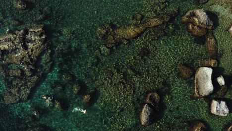 Aerial-drone-shot-of-the-ocean-coastline-scattered-with-rocks-and-swimmer-with-snorkle