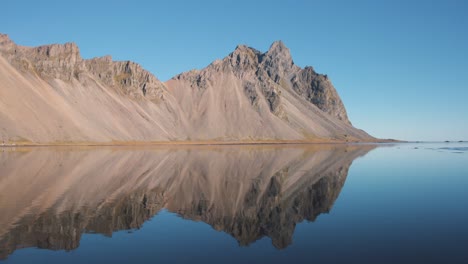 Sharp-Vestrahorn-mountain-peak-reflecting-in-still-sea-water-below