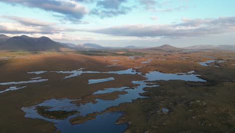 Wide-drone-shot-of-Connemara-Lakes-with-calm-lakes-in-the-foreground-and-Beanna-Beola-mountain-range-in-the-distance,-slowly-panning-aerial-shot