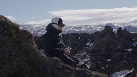 Mann-Sitzt-Und-Fliegt-FPV-Drohne-Mit-Schutzbrille-Durch-Malerische-Vulkanlandschaft