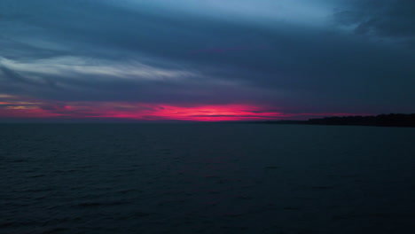 Final-pink-red-glow-emits-behind-clouds-above-calm-water-at-dusk