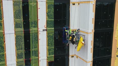 Aerial-view-of-worker-team-in-lift-working-on-outside-facade-of-skyscraper-building