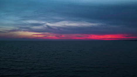 Aerial-dolly-out-to-sunset's-last-light-of-pink-red-hues-above-water