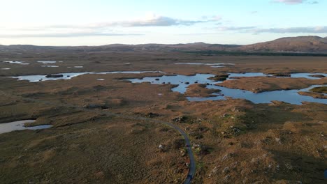 Wide-drone-shot-of-Connemara-Lakes-with-road-and-small-calm-lakes-in-the-foreground-and-Beanna-Beola-mountain-range-in-the-distance,-slow-revealing-aerial-shot