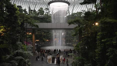 A-static-shot-of-the-world's-tallest-indoor-waterfall-called-the-Vortex-at-Jewel-Changi-Airport,-below-people-go-about-their-day,-Singapore