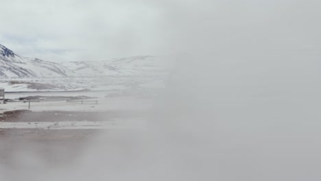 Un-Turista-Vestido-De-Negro-Se-Encuentra-Detrás-De-Una-Densa-Nube-De-Vapor-En-El-Paisaje-De-Islandia