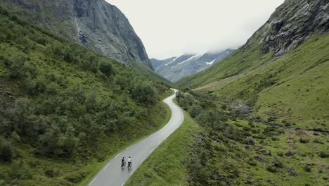 Aerial-drone-shot-of-cyclists-cycling-down-mountain-road-pass-with-dramatic-scenery-in-the-background