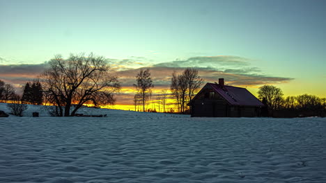 Timelapse-shot-of-sun-setting-through-clouds-behind-beautiful-wooden-cottage-surrounded-by-thick-layer-of-white-snow-on-a-winter-evening