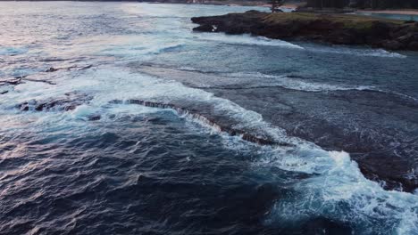 Water-forming-white-froth-as-tide-rolls-into-remote-bay-at-sunset,-aerial