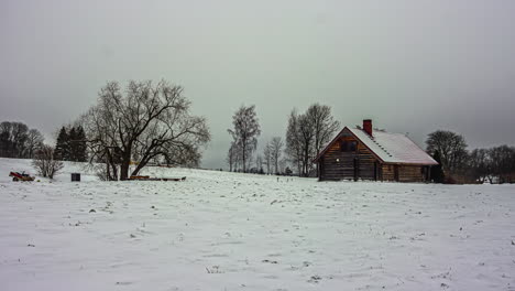 Timelapse-shot-of-dark-cloud-movement-over-a-wooden-cottage-surrounded-by-thick-layer-of-white-snow-on-a-winter-day