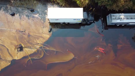 Semi-trucks-trapped-in-deep-flooded-mudslide-with-oil-spill-along-riverbank