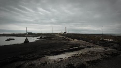 aerial-beach-footpath-leading-to-lighhouse-on-grotta-island,-reykjavik-iceland,-dark-cloudy-moody-scenery