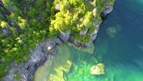 Rocky-coastline-with-forest-and-crystal-clear-lake-water,-aerial-top-down-view