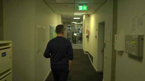 White-man-walking-through-corridor-of-corporate-office-building-to-control-room