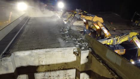 Vista-Aérea-De-Maquinaria-Pesada-Demoliendo-Un-Antiguo-Puente-De-Carretera,-Por-La-Noche