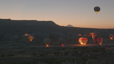 Heißluftballons-Erhellen-Den-Startbereich-Am-Frühen-Morgen-In-Der-Dunklen-Landschaft